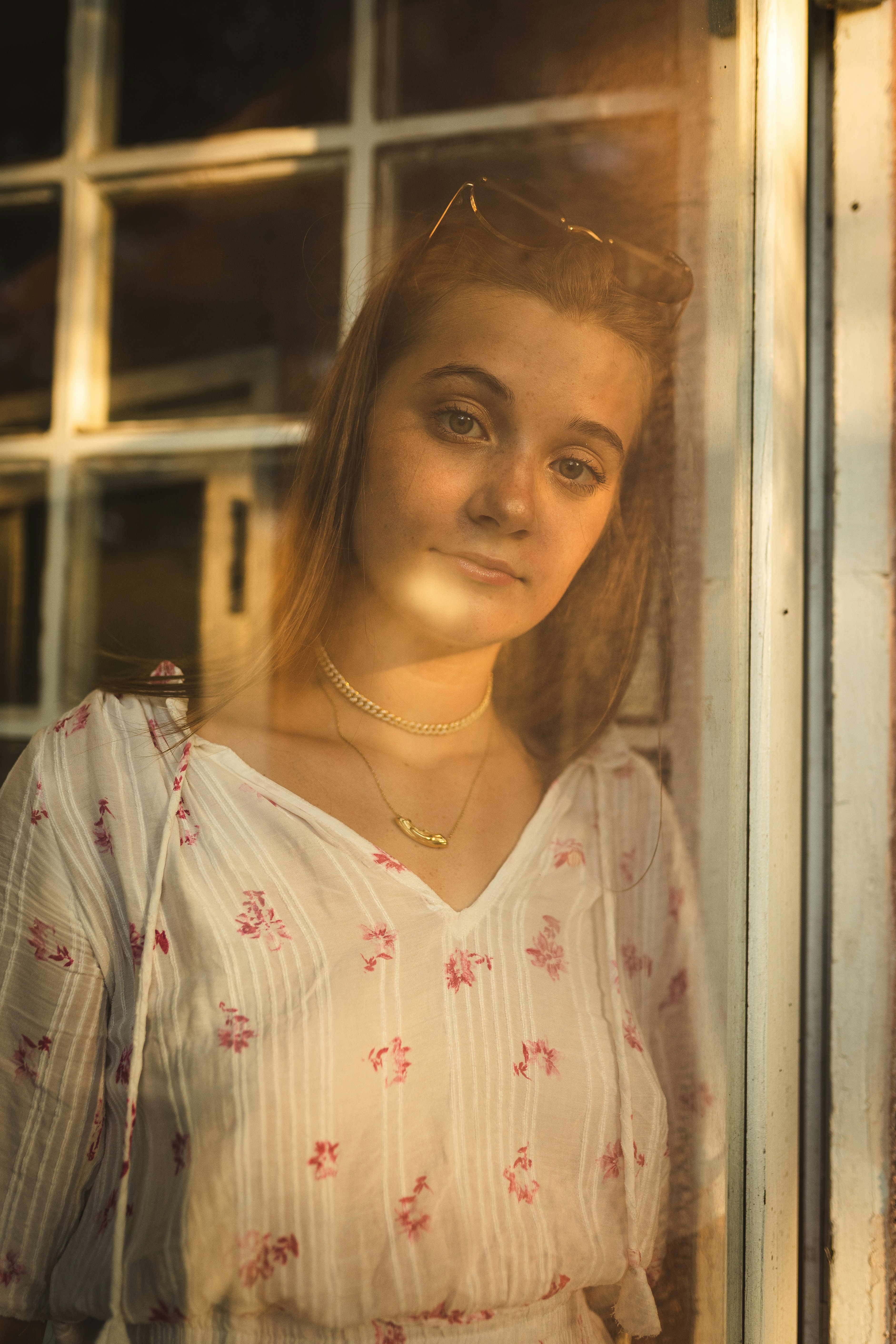 woman in white and red floral shirt standing beside glass window